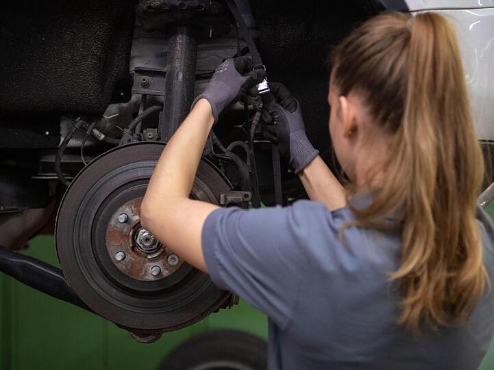 Eine Kfz-Mechanikerin wechselt in einer Werkstatt die Bremsscheibe eines Autos.