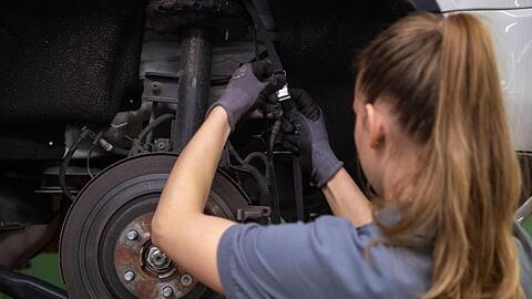 Eine Kfz-Mechanikerin wechselt in einer Werkstatt die Bremsscheibe eines Autos.