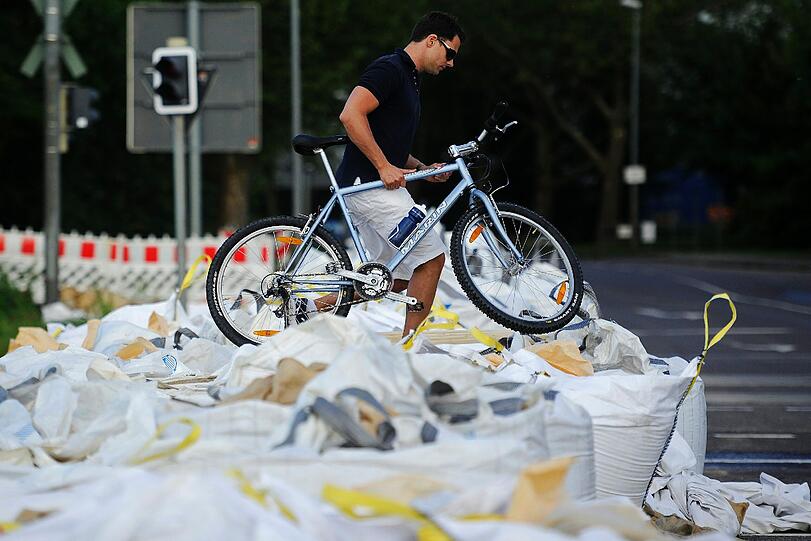 Ein Mann trägt am 10.06.2013 in Magdeburg sein Fahrrad über eine Barriere aus Sandsäcken.