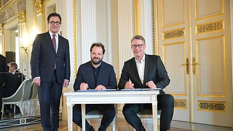 Im K&ouml;nigssaal des Nationaltheaters hat Popelka (m.) nun mit Bayerns Kunstminister Markus Blume (r.) den Vertrag unterschrieben, zur Freude von Staatsintendant Serge Dorny (l.)