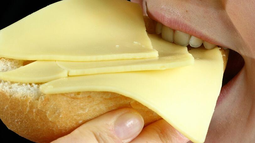 Eine Frau beißt in ein mit Käse belegtes Brötchen. (Symbolbild)