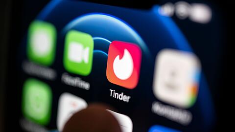 Ein Finger bedient ein Smartphone auf dem unter anderen die App von Tinder installiert ist.