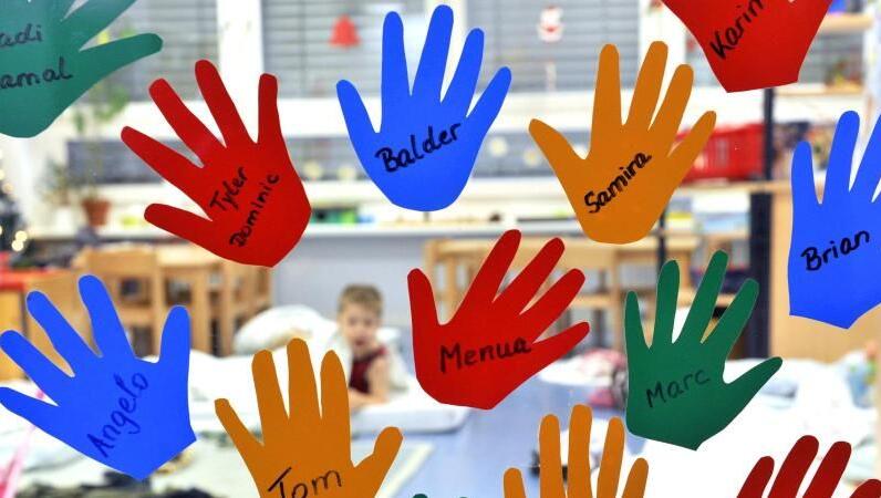 Aus Folien geschnittene Kinderhände hängen mit den jeweiligen Namen an der Eingangstür einer Kindergruppe in einer Tagesstätte. Aus Folien geschnittene Kinderhände hängen mit den jeweiligen Namen an der Eingangstür einer Kindergruppe in einer Tagesstätte.