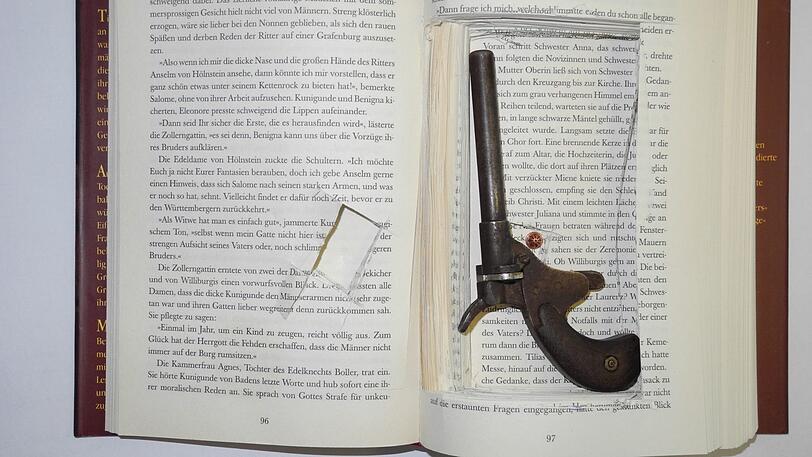 Pistole im Buch: Dieser Trick hätte vielleicht in den 60er Jahren funktioniert. Die Technik hat sich allerdings weiterentwickelt.