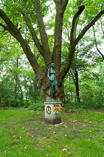 "Das Bild zeigt eine Statue in den Frühlingsanlagen an der Isar zwischen der Eduard-Schmitt-Straße und der Reichenbachbrücke. Leider weiß ich den Namen des Mädchens nicht, obwohl ich im Sommer sicher zwei bis dreimal die Woche vorbeigehe. Das Bild wirkt durch den Schriftzug 'Denk mal' natürlich erst interessant. Es beschreibt das Künstlerische das in den letzten Jahren von dem Glockenbachviertel in die Au 'rüberschwappt"'.