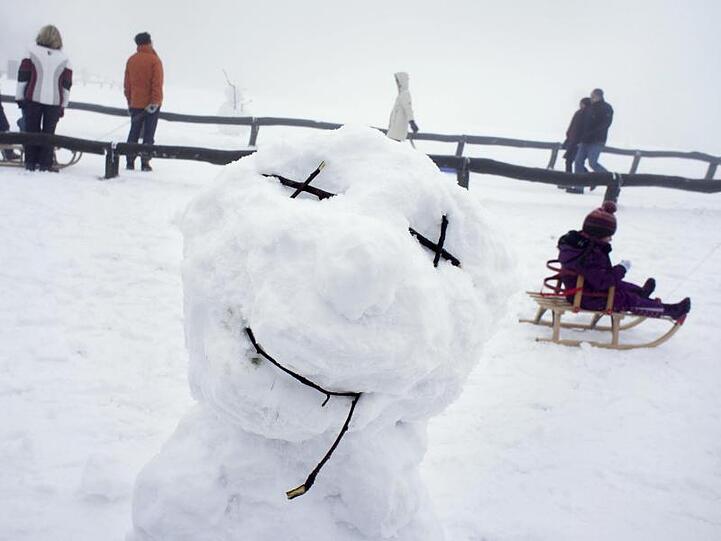 Ein Schneemann steht auf dem Gipfelplateau des Großen Feldbergs zwischen den Ausflüglern mit ihren Schlitten. Foto: Frank Rumpenhorst/Archiv