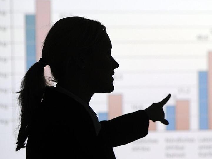 Eine Frau erklärt eine mittels Beamer an die Wand projizierte Statistik. Foto: picture alliance / dpa/Illustration