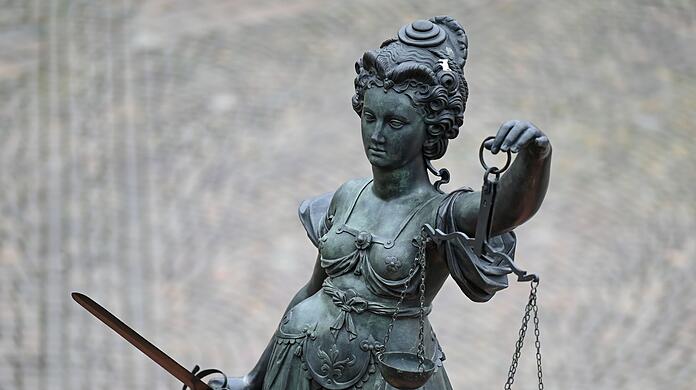 Eine Statue der Justitia hält eine Waage und ein Schwert in der Hand.