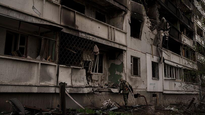 Ein ukrainischer Soldat steht nach einem russischen Angriff vor einem beschädigten Wohnhaus.