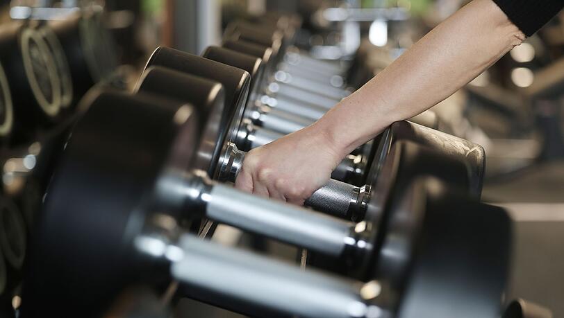 Eine Frau nimmt in einem Fitnessstudio Hanteln aus dem Ständer.