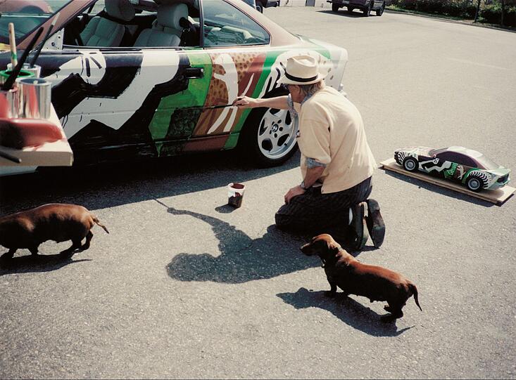 Bei den beiden Dackeln dürfte es sich um Stanley und Little Boodge handeln. David Hockney hatte die beiden überall dabei und nahm sie sogar mit ins Bett. Dagegen war so ein Art Car eher unbequem. Aber die Burschen schien das 1995 eh nicht zu interessieren. Und Herrchen beim Malen kannten sie ja. Das heißt, beim Malen von Swimmingpool-Bildern. Hockney dachte sich für den BMW 850 CSi etwas Besonderes aus: Er übertrug die Innenwelt des Autos nach außen, so, als ob man hineinsehen könnte. Auf der Tür ist der Fahrer schemenhaft zu erkennen, auf dem Rücksitz Dackel Stanley. Bei den beiden Dackeln dürfte es sich um Stanley und Little Boodge handeln. David Hockney hatte die beiden überall dabei und nahm sie sogar mit ins Bett. Dagegen war so ein Art Car eher unbequem. Aber die Burschen schien das 1995 eh nicht zu interessieren. Und Herrchen beim Malen kannten sie ja. Das heißt, beim Malen von Swimmingpool-Bildern. Hockney dachte sich für den BMW 850 CSi etwas Besonderes aus: Er übertrug die Innenwelt des Autos nach außen, so, als ob man hineinsehen könnte. Auf der Tür ist der Fahrer schemenhaft zu erkennen, auf dem Rücksitz Dackel Stanley.
