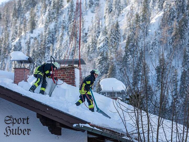 Feuerwehrleute räumen auf einem Haus in Bayrischzell im Grenzgebiet zu Österreich Schnee von einem Dach. Foto: Christoph Reichwein