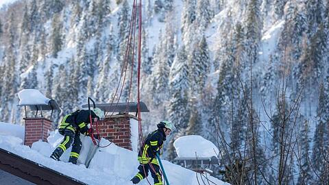 Feuerwehrleute räumen auf einem Haus in Bayrischzell im Grenzgebiet zu Österreich Schnee von einem Dach. Foto: Christoph Reichwein