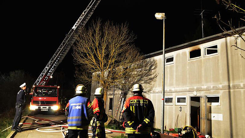 Einsatzkräfte von Feuerwehr und Polizei stehen in Weil der Stadt vor der Flüchtlingsunterkunft, in der das Feuer ausgebrochen war.