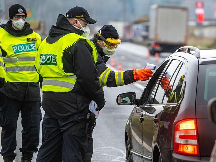 Ein Feuerwehrmann aus Tschechien misst neben Polizisten die Temperatur von einem Einreisenden an der Grenze.