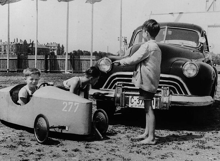 Was ist jetzt schöner - das kleine Rennauto oder der Schlitten der Amis? Die Frage stellen sich offenbar auch diese Burschen in den 50ern.