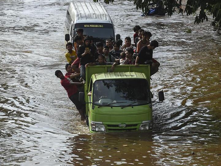 Menschen stehen auf der Ladefläche eines Transporters, um eine überflutete Straße in Jakarta zu passieren.