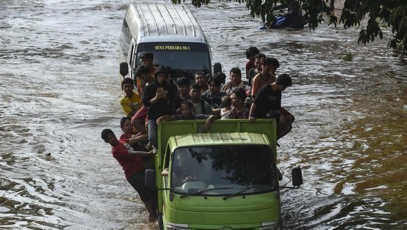 Menschen stehen auf der Ladefläche eines Transporters, um eine überflutete Straße in Jakarta zu passieren. Menschen stehen auf der Ladefläche eines Transporters, um eine überflutete Straße in Jakarta zu passieren.