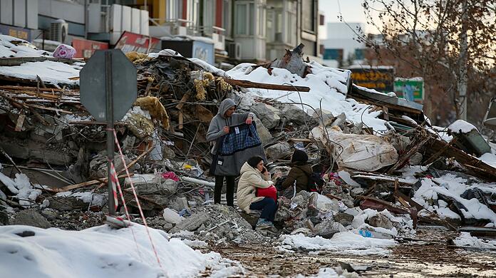 Erdbebenkatastrophe in der Türkei und Syrien: Menschen sitzen zwischen den Trümmern vor einem eingestürzten Gebäude.