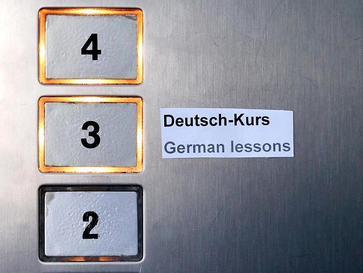 Ein Schild "Deutsch-Kurs" und "German lessons" klebt im Fahrstuhl eines Gebäudes. Foto: Jan Woitas/dpa-Zentralbild/dpa/Symbolbild