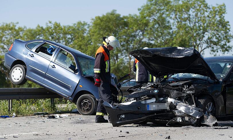 Feuerwehrleute stehen am 27.07.2013 auf der A96 bei Landsberg am Lech neben einem Unfallfahrzeug. Zuvor war ein 76-jähriger Rentner in den BMW eines entgegenkommenden Mannes gefahren.