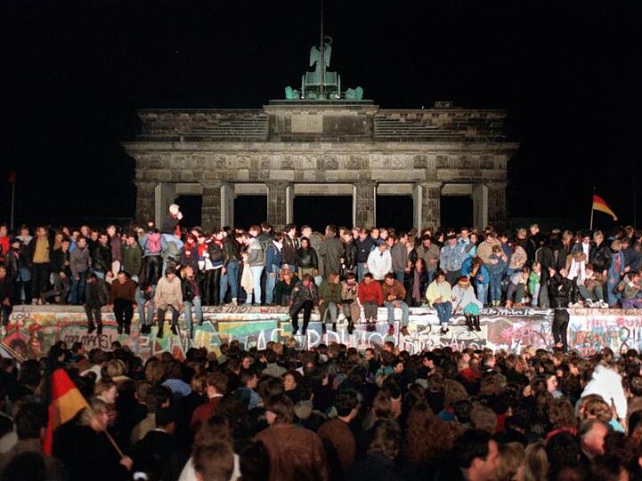Jubelnde Menschen sitzen nach der Maueröffnung auf den Grenzanlagen am Brandenburger Tor.