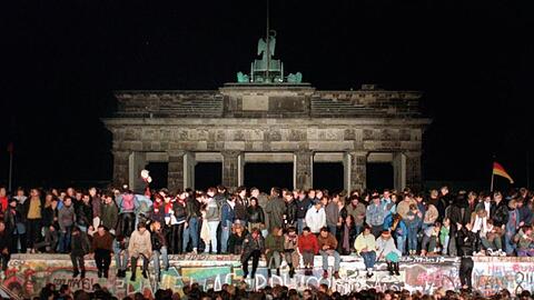 Jubelnde Menschen sitzen nach der Maueröffnung auf den Grenzanlagen am Brandenburger Tor.