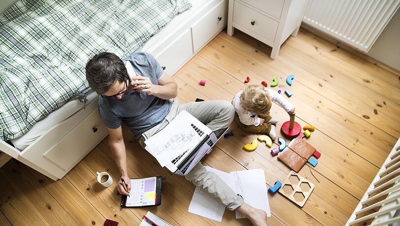 Das Homeoffice birgt einige Tücken: Stolpert dieser Mann während der Arbeitszeit über die bunten Scheiben, mit denen das Kind spielt, ist er nicht versichert