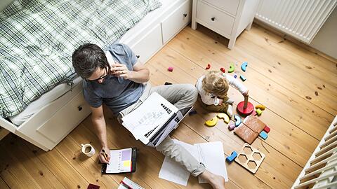 Das Homeoffice birgt einige Tücken: Stolpert dieser Mann während der Arbeitszeit über die bunten Scheiben, mit denen das Kind spielt, ist er nicht versichert