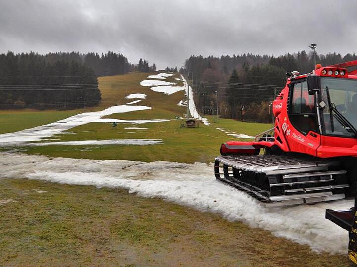 Eine Pistenraupe steht auf einer Skipiste, die nur noch teilweise mit Schneeresten bedeckt ist. Foto: Benjamin Liss/dpa/Symbolbild