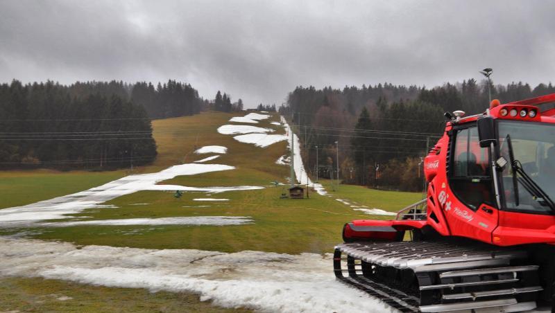 Eine Pistenraupe steht auf einer Skipiste, die nur noch teilweise mit Schneeresten bedeckt ist. Foto: Benjamin Liss/dpa/Symbolbild