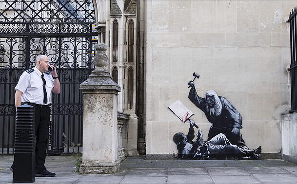Ein undatiertes, von Banksy veröffentlichtes Foto des neuen Kunstwerks des Künstlers, das einen Richter zeigt, der einen Demonstranten mit einem Hammer vor den Royal Courts of Justice in London schlägt.