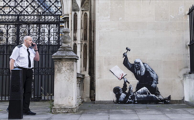 Ein undatiertes, von Banksy veröffentlichtes Foto des neuen Kunstwerks des Künstlers, das einen Richter zeigt, der einen Demonstranten mit einem Hammer vor den Royal Courts of Justice in London schlägt.