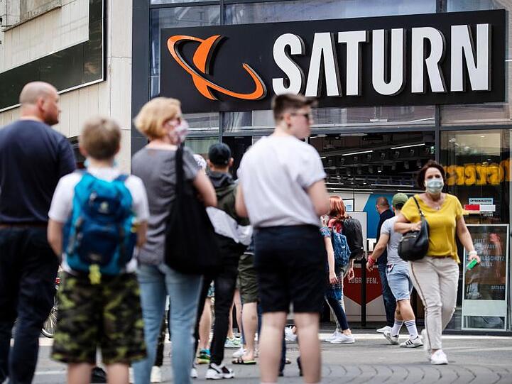 Menschen stehen in einer Warteschlange in Köln vor einer Filiale des Elektrohändlers Saturn an.