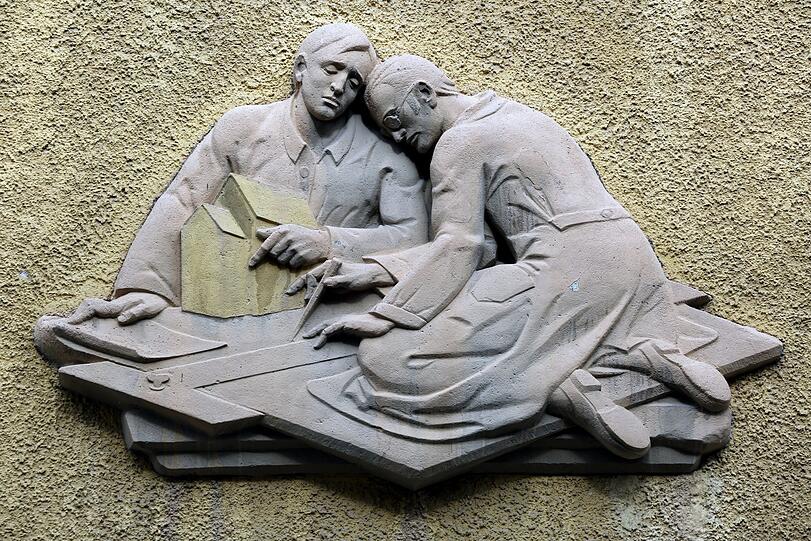 Kunst am Bau: Szenen aus dem Bauhandwerk schmücken die Gebäude in der Enzenspergerstraße: Erst wird geplant, dann gesägt und schließlich aufgemauert.