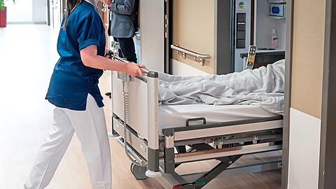 Pflegepersonal schiebt einen Patienten ins Krankenzimmer.