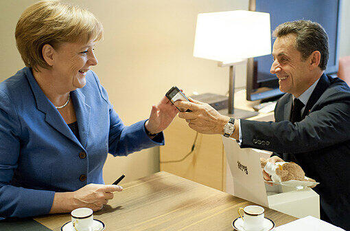 Baby-Geschenk: Angela Merkel überreicht Sarkozy hinter den Kulissen einen Teddybären für die kleine Giulia.