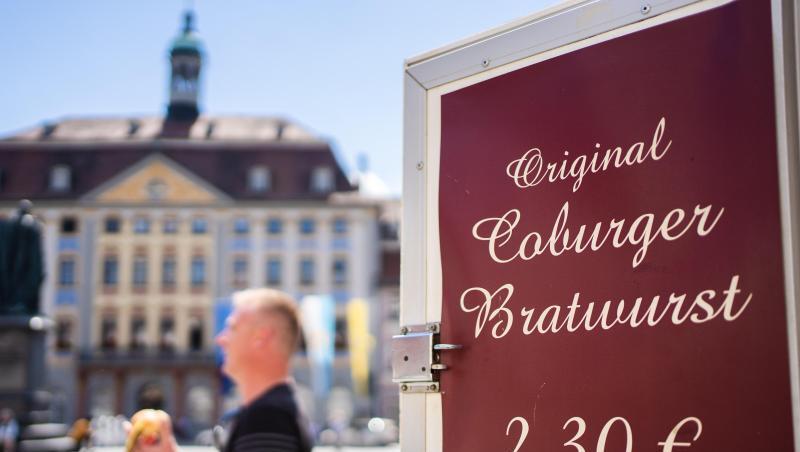 Ein Mann geht auf Coburger Marktplatz an Schild mit Aufschrift "Original Coburger Bratwurst" vorbei. Foto: Nicolas Armer/dpa Ein Mann geht auf Coburger Marktplatz an Schild mit Aufschrift "Original Coburger Bratwurst" vorbei. Foto: Nicolas Armer/dpa