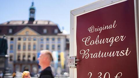 Ein Mann geht auf Coburger Marktplatz an Schild mit Aufschrift "Original Coburger Bratwurst" vorbei. Foto: Nicolas Armer/dpa