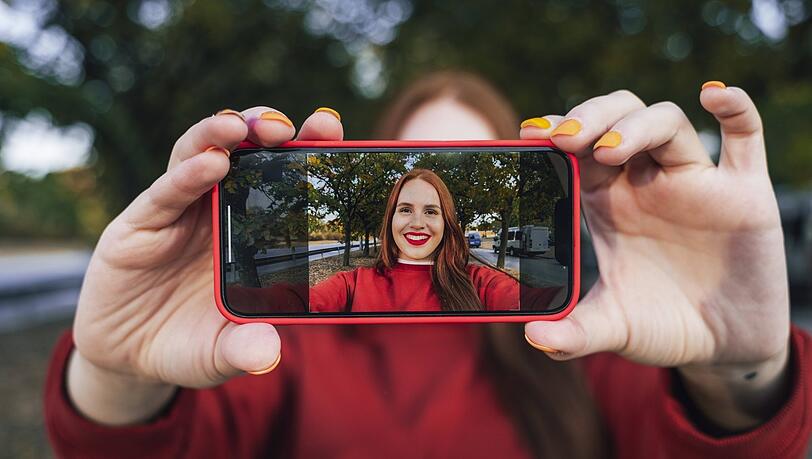 Eine junge Frau filmt sich mit dem Handy selbst. Influencer können Politiker, Sportler, Journalisten, Blogger, YouTuber, Prominente und Schauspieler sein, die mit ihren Internet-Beiträgen durch Werbung Geld verdienen – oft sehr ordentlich.
