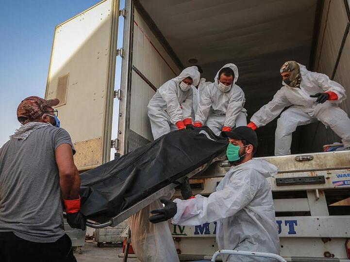 Arbeiter in Schutzkleidung beladen in Bagdad einen Kühlwagen mit Leichen von Menschen, die am Coronavirus gestorben sind.