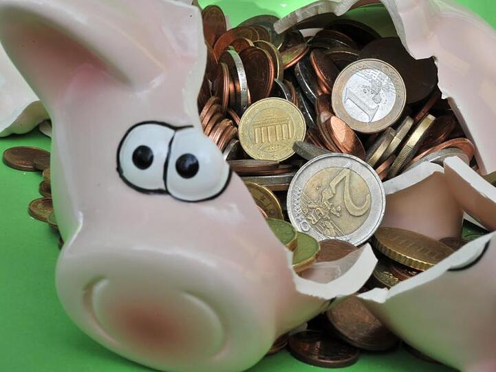 Ein Sparschwein mit Euro-Geldstücken liegt zerbrochen auf einem Tisch. Foto: Peter Kneffel/Archiv