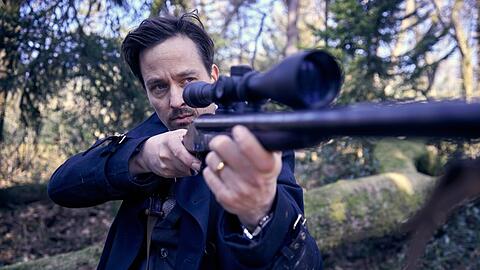 "Der Pfau": Andreas (Tom Schilling) hat ein Gewehr im Wald gefunden und richtet es auf seine Team-Mitglieder.