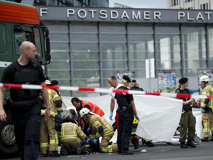 Rettungskräfte helfen auf der Straßenkreuzung am Potsdamer Platz in Berlin einem verletzten Radfahrer, der unter einem Lastwagen liegt.