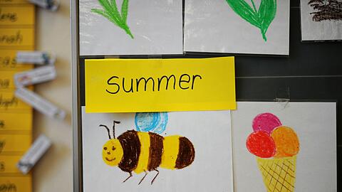 Bunte Zeichnungen und das englische Wort "summer" hängen in einer Grundschule.