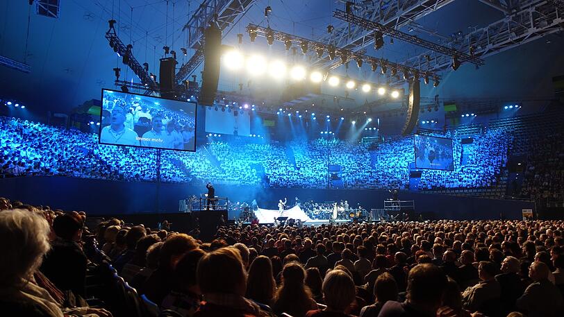 Reformation im musikalischen Großformat: Im Tribünenrund hinter der Bühne: der Chor der 2000. Auf den Podesten die beiden Chordirigenten, in der Mitte die Schauplatz-Bühne und dahinter Orchester und Band.