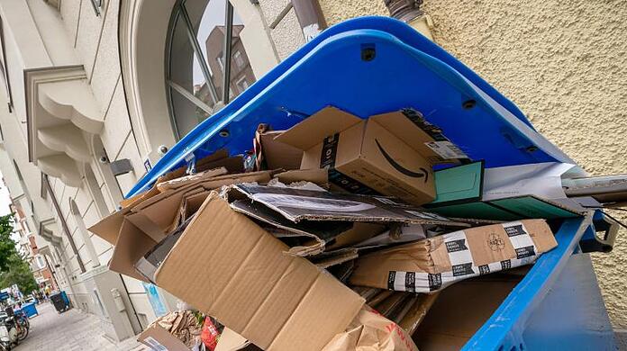 Ein Übervoller Papierkontainer steht vor einem Haus zur Abholung durch die Müllabfuhr bereit.