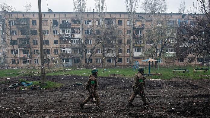 Ukrainische Soldaten gehen in Bachmut an stark beschädigten Gebäuden vorbei.