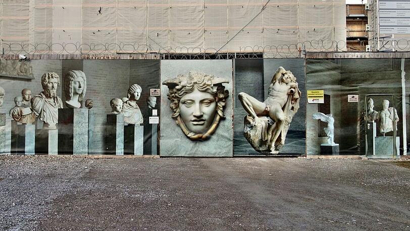 Vor der Glyptothek steht Münchens schönster Bauzaun. Der zeigt, was man derzeit vermisst. Doch es gibt eine gute Nachricht: Das Haus öffnet im Herbst früher als geplant, und die Sanierungskosten werden nicht überschritten.
