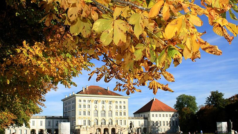 Passanten und Spaziergänger geniessen die warmen Sonnenstrahlen und das bunte Herbstlaub bei einem Spaziergang oder sitzen auf einer Parkbank in der Sonne im Schlosspark Nymphenburg in München Passanten und Spaziergänger geniessen die warmen Sonnenstrahlen und das bunte Herbstlaub bei einem Spaziergang oder sitzen auf einer Parkbank in der Sonne im Schlosspark Nymphenburg in München